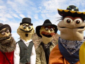 The Banana Kid and fellow cowboy puppets against a blue cloudy sky. Come see us at Puppets Up!